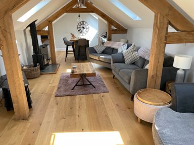 An attic living room with wooden beams two sofas a coffee table a wood burning stove a dining table with chairs and skylights at Lugg View Cross Keys near Hereford