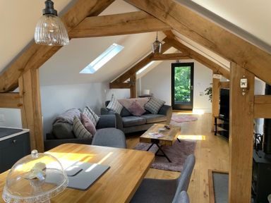 An attic living space with wooden beams sofas a coffee table TV and a dining table at Lugg View in Cross Keys near Hereford