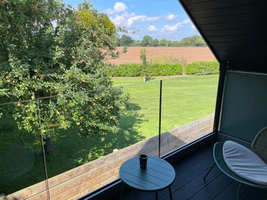 A balcony with a round table and chair overlooking a garden with an apple tree and fields at Lugg View in Cross Keys near Hereford