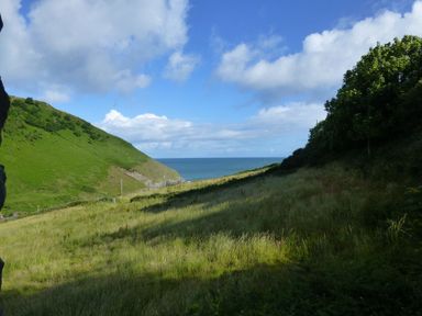 A grassy valley between hills with the sea in the distance at Dolwylan Cottage in Cwmtydu near New Quay