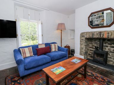 A living room with a blue sofa, wooden table, and a fireplace at Dolwylan Cottage in Cwmtydu near New Quay