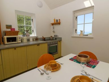 A kitchen with cabinet and dining table at Dolwylan Barn Cwmtydu near New Quay
