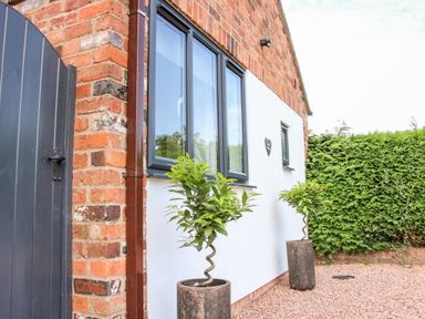 Exterior of a brick and white wall building with black window frames two potted plants gravel ground and a green hedge at Oakleigh in Four Crosses
