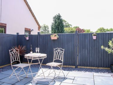 A patio with a small round table and two chairs against a dark wooden fence with hanging flower pots at Oakleigh in Four Crosses