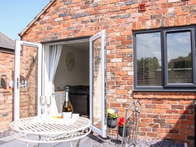 A brick exterior wall with an open glass door leading to a room and a white metal table with a bottle and glasses outdoors at Oakleigh in Four Crosses
