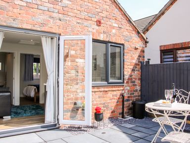 A patio with a small table and two chairs outside a brick house with an open door and window at Oakleigh in Four Crosses