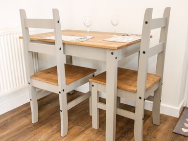 A wooden dining table set with two chairs on a wooden floor with place mats and wine glasses at Oakleigh in Four Crosses