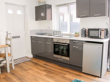 A kitchen with grey cabinets white countertop oven microwave kettle and small fridge at Oakleigh in Four Crosses
