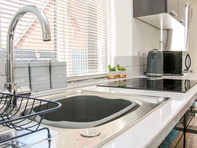 A kitchen sink with a drying rack near a window with blinds and containers labeled sugar coffee and tea along with a kettle and microwave on the countertop at Oakleigh in Four Crosses