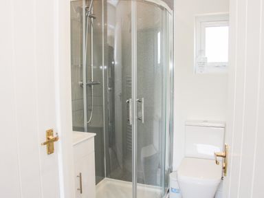 A small bathroom with a glass shower enclosure a toilet and a small window at Oakleigh in Four Crosses