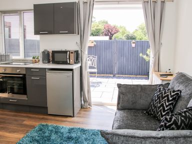 A kitchen with gray cabinets a microwave kettle and oven next to a gray sofa with patterned cushions and a sliding door to a patio at Oakleigh in Four Crosses