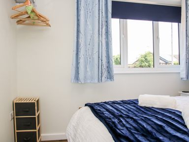 A bedroom with a bed covered with a blue blanket and white towel next to a window with blue patterned curtains and wooden hangers on the wall at Oakleigh in Four Crosses