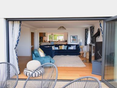 A living room with blue sofas and patterned curtains next to a wood stove at Ty Ni in New Quay