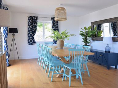 A dining room with a wooden table surrounded by light blue chairs and blue patterned curtains at Ty Ni in New Quay