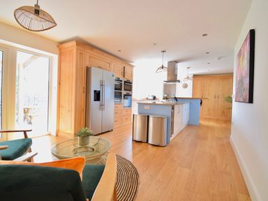 A kitchen with wooden cabinets and stainless steel appliances with a seating area and glass door at Ty Ni in New Quay