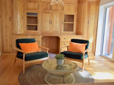 A sitting area with two armchairs and a round coffee table on a circular rug in front of wooden cabinets at Ty Ni in New Quay