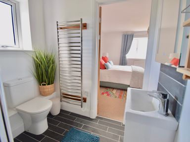 A bathroom with a toilet a sink a towel radiator and a plant seen through an open door to a bedroom at Ty Ni in New Quay