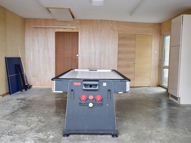 A game room with an air hockey table a folded ping pong table wooden paneled walls and a concrete floor at Ty Ni in New Quay