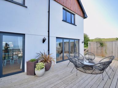 An outdoor wooden deck with black metal chairs around a glass table and potted plants at Ty Ni in New Quay