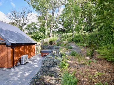 A garden with a wooden shed a stone path and plants surrounded by trees at Ty Ni in New Quay