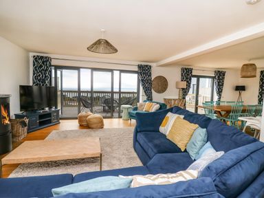A living room with blue sofas pillows a coffee table TV and sliding glass doors opening to a balcony at Ty Ni in New Quay