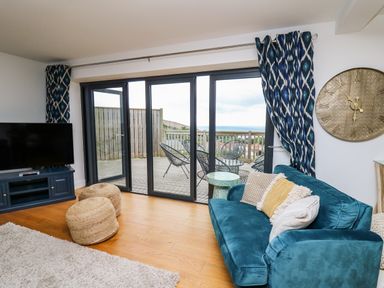 A living room with a blue sofa pillows large clock sliding glass doors and balcony at Ty Ni in New Quay