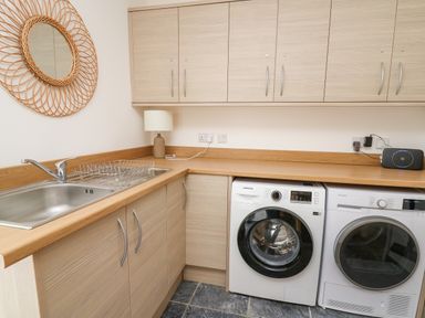 A laundry room with a stainless steel sink washing machine dryer and wooden cabinets at Ty Ni in New Quay