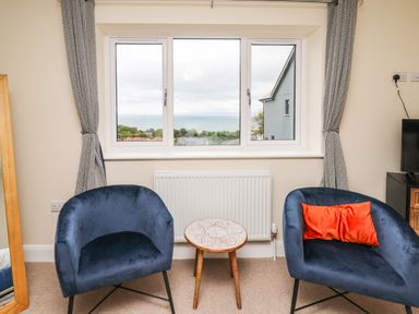 A room with two blue chairs and a small round table between them in front of a window with curtains at Ty Ni in New Quay