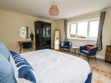 A bedroom with a bed pillows a black wardrobe two blue chairs a brown table a standing mirror and a dressing table at Ty Ni in New Quay