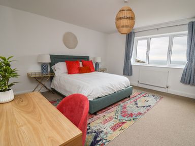 A bedroom with a bed with red pillows a wooden desk a red chair and a large window at Ty Ni in New Quay