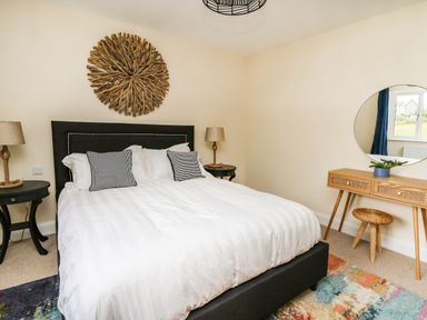 A bedroom with a large bed white bedding two striped pillows two bedside tables with lamps a wooden dressing table a round mirror and a wall decoration at Ty Ni New Quay