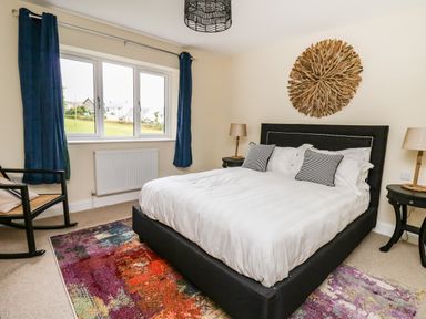 A bedroom with a bed white bedding two bedside tables with lamps a wooden wall decoration and a colorful rug at Ty Ni in New Quay