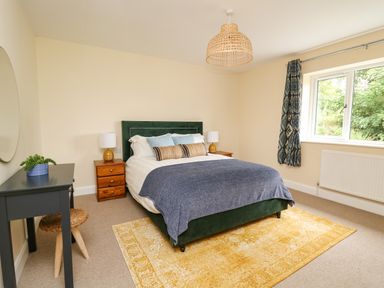 A bedroom with a green bed on a yellow rug beside a window with patterned curtains at Ty Ni in New Quay