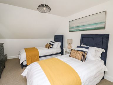 A bedroom with two single beds yellow throws pillows a lamp and a painting at Ty Ni in New Quay