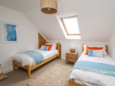 A bedroom with two single beds a wooden nightstand under a skylight window and a patterned rug on the floor at Ty Ni in New Quay