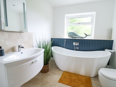 A bathroom with a freestanding bathtub a sink with mirror and a potted plant at Ty Ni in New Quay