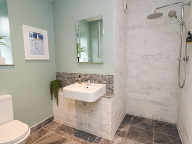A bathroom with a toilet, wall-mounted sink, mirror, and a shower area with two showerheads at Ty Ni in New Quay
