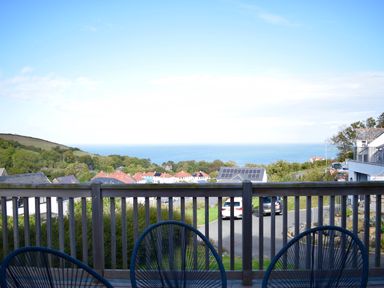 A balcony with chairs overlooking houses trees a hill and the sea at Ty Ni in New Quay