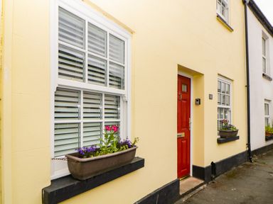 A yellow house exterior with white windows, flower boxes, and a red door at The Yellow House 13 King Street in Dawlish