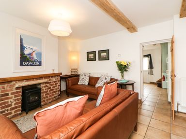 A living room with two brown leather sofas a brick fireplace with a small black stove a wooden side table with flowers and framed pictures on the wall at The Yellow House 13 King Street in Dawlish