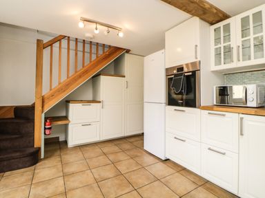 A kitchen with white cabinets a microwave oven fridge and a wooden staircase at The Yellow House 13 King Street in Dawlish