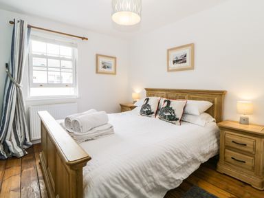 A bedroom with a wooden bed white bedding swan cushions bedside tables with lamps and a window with striped curtains at The Yellow House 13 King Street in Dawlish
