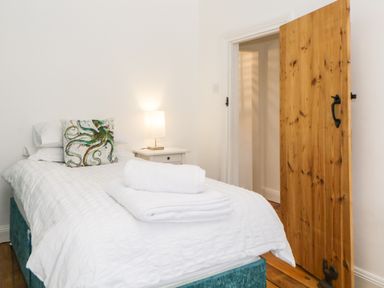 A bedroom with a single bed with white bedding and towels a wooden door and a bedside table with a lamp at The Yellow House 13 King Street in Dawlish