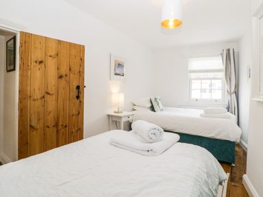 A bedroom with two single beds bedside table lamp wooden door and window at The Yellow House 13 King Street in Dawlish