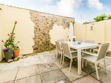 An outdoor patio with a table, chairs, potted plants, and a partially exposed stone wall at The Yellow House in Dawlish