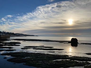 A coastal scene at sunset with rock formations in the water and buildings along the shore at The Yellow House 13 King Street in Dawlish