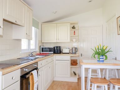 A kitchen with cream cabinets a wooden countertop appliances and a table with yellow flowers at 224 Atlantic Bays in St Merryn