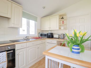 A kitchen with cream cabinets a sink a microwave toaster kettle and yellow flowers in a striped vase on a table at 224 Atlantic Bays in St Merryn