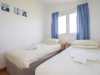 A bedroom with two single beds a small wooden bedside table with a lamp and blue curtains at 224 Atlantic Bays in St Merryn