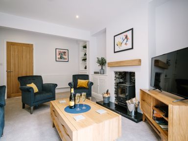 A living room with blue armchairs a wooden coffee table a fireplace and a television at Craig Cottage in Bowness-On-Windermere